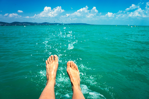 A happy girl woman is kicking feet on a sea lake and splashing water on a sail boat summertime holiday