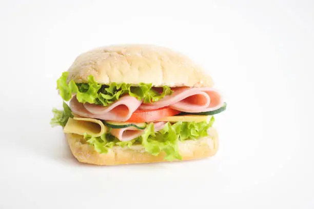 Sandwich on a white background. At the heart of the mini ciabatta sandwich. A filling of slices of ham, cheese, lettuce, fresh cucumbers and tomatoes. Close-up.
