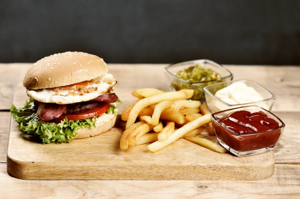 istock Hamburger on a light wooden board. The burger includes bacon, fried egg and dried onions. Next to the burger are french fries and cups with sauces. 1155511665