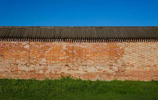 Brick wall with a wooden roof against the sky and green grass