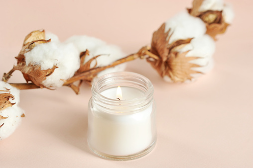 A cotton flower and a white candle in a glass jar. Beige background. Close-up. Macro shooting.