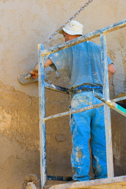 volunteer applying adobe (mud) to a church wall. - ranchos de taos imagens e fotografias de stock