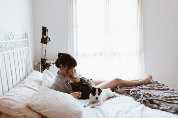 istock Brunette woman playing with puppy while lying on bed at bedroom 1155523772