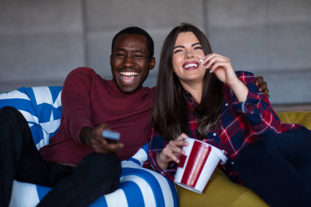 retrato de una joven pareja sentada en el sofá viendo una película con expresión en sus rostros - couple young adult african descent multi ethnic group fotografías e imágenes de stock