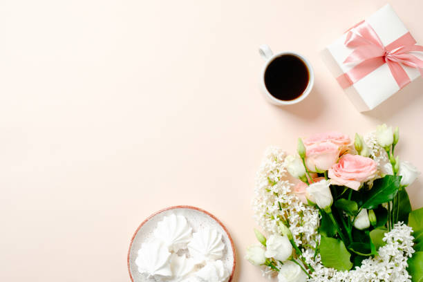 istock Flat lay home office desk. Female workspace with coffee cup, gift box, marshmallows and bouquet of roses on pink background. Top view feminine background with copy space for text. 1155525734