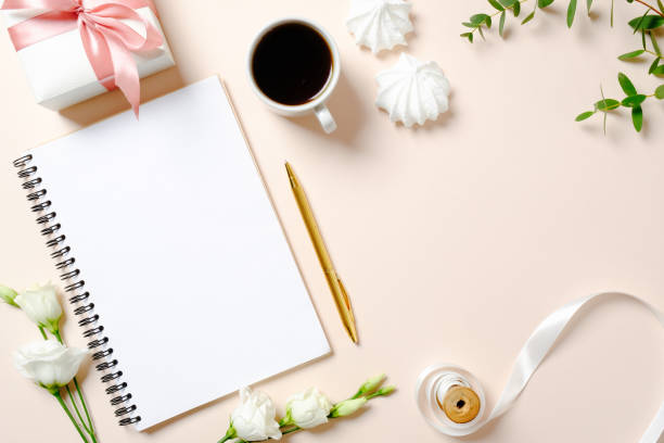 istock Flat lay home office desk. Female workspace with blank paper notebook, coffee cup, gift box, marshmallows and roses flowers on pink background. Top view feminine background with copy space for text. 1155525750