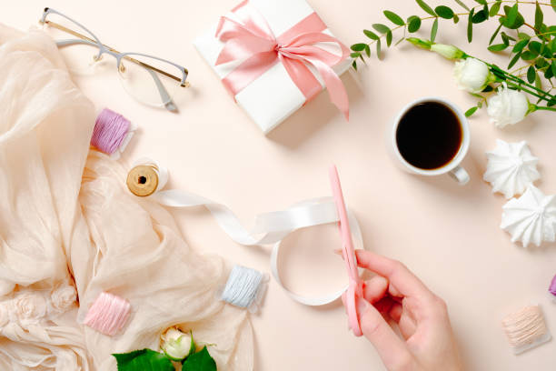 Flat lay, top view feminine desk with coffee cup, flowers, marshmallows, gift box and spools with ribbon on pink background. Festive home office desk concept, female workspace with girl's accessories flat lay, escritorio femenino de vista superior con taza de café, flores, malvaviscos, caja de regalo y carretes con cinta sobre fondo rosa. concepto de escritorio de oficina en casa festiva, espacio de trabajo femenino con accesorios de niña