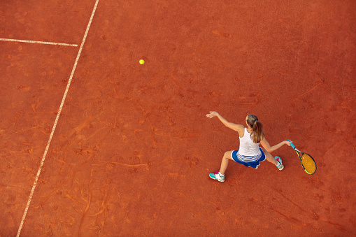 Aerial shot of a female tennis player on a court during match. Young woman playing tennis. High angle view