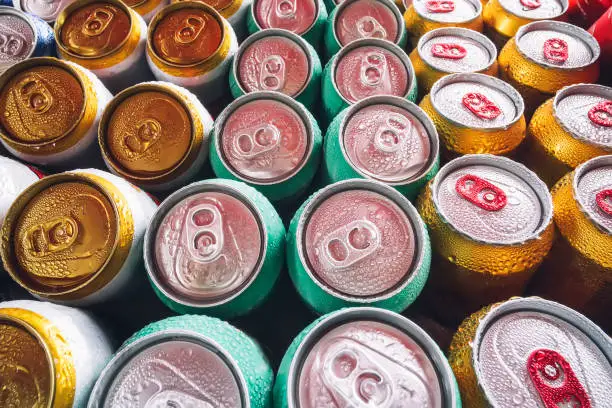 Photo of Lots of aluminum cans in the ice in the open fridge. Drops of water on a cold can of drink. Metal cans of beer with ice cubes in mini refrigerator, close up