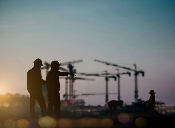 istock silhouette engineer looking Loaders and trucks in a building site over Blurred construction worker on construction site 1155534215