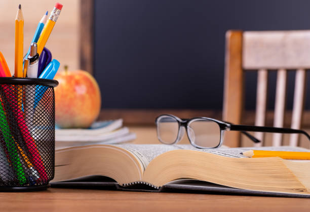 Closeup of an opened book on a school desk with a blank blackboard for copy space in background