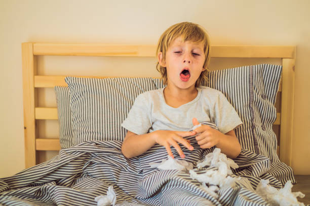 Sick boy coughs and wipes his nose with wipes. Sick child with fever and illness in bed Sick boy coughs and wipes his nose with wipes. Sick child with fever and illness in bed. snorting stock pictures, royalty-free photos & images