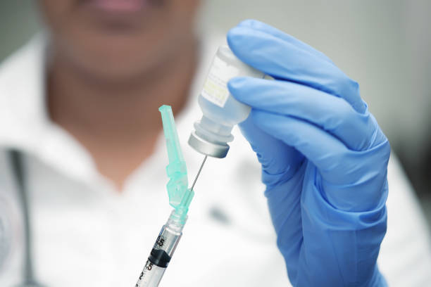 Medical professional with white scrubs and blue nitrile gloves, preparing a vaccine shot. stock photo