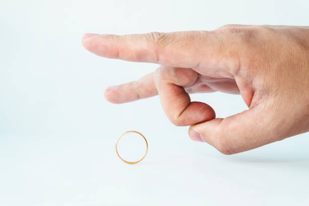 Divorce concept. Male hand kicking wedding ring on white background. Relationship breakup. Unfaithful spouse. Person pulls off the golden ring. Not wishing to stay married anymore. Parting of couple Divorce concept. Male hand kicking wedding ring on white background. Relationship breakup. Unfaithful spouse. Person pulls off the golden ring. Not wishing to stay married anymore. Parting of couple. divorcee stock pictures, royalty-free photos & images