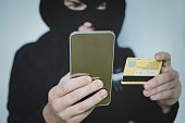 Cyber criminal in balaclava enters the information of a personal bank account. Credit card fraudulent scheme. Stealing cyber money using mobile. New ways of fraudulent transactions via online banking