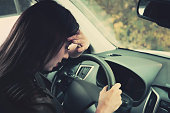 Woman driver feeling anxiety behind the wheel. Close up of crying girl sitting inside vehicle and crying. Female driver felt headache and sickness driving. Woman closed eyes and touches her forehead.