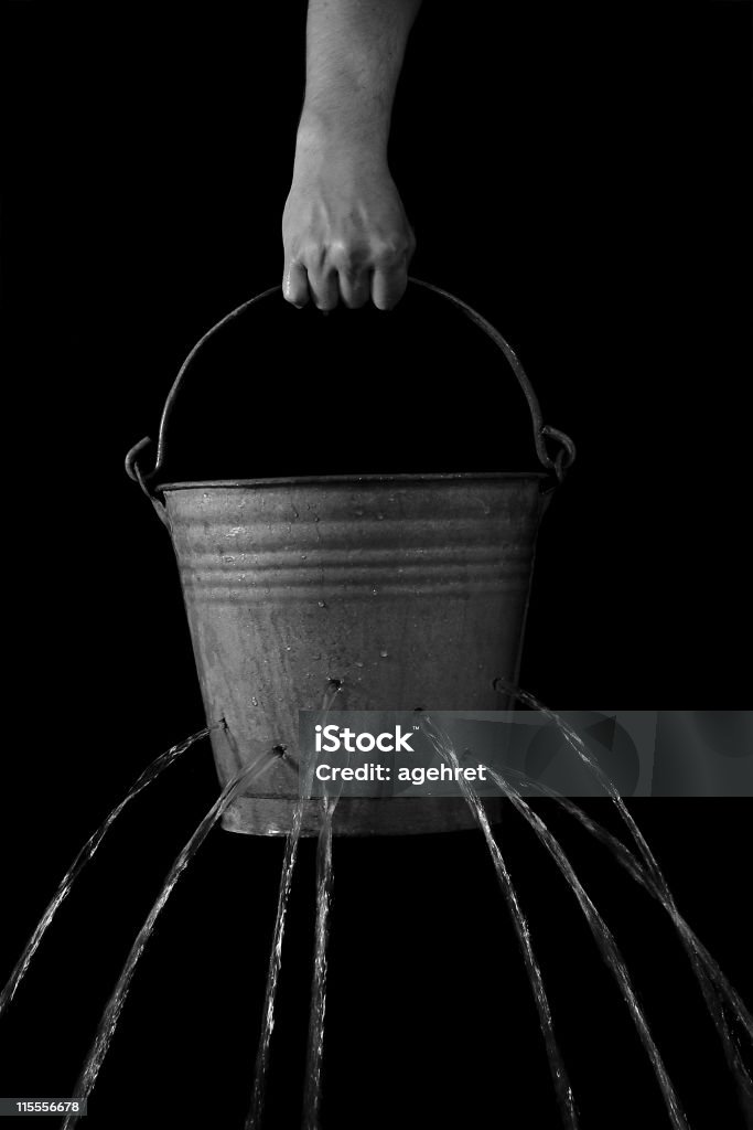 In vain Water bucket with holes loosing water, held by a man. Black background Leaking Stock Photo