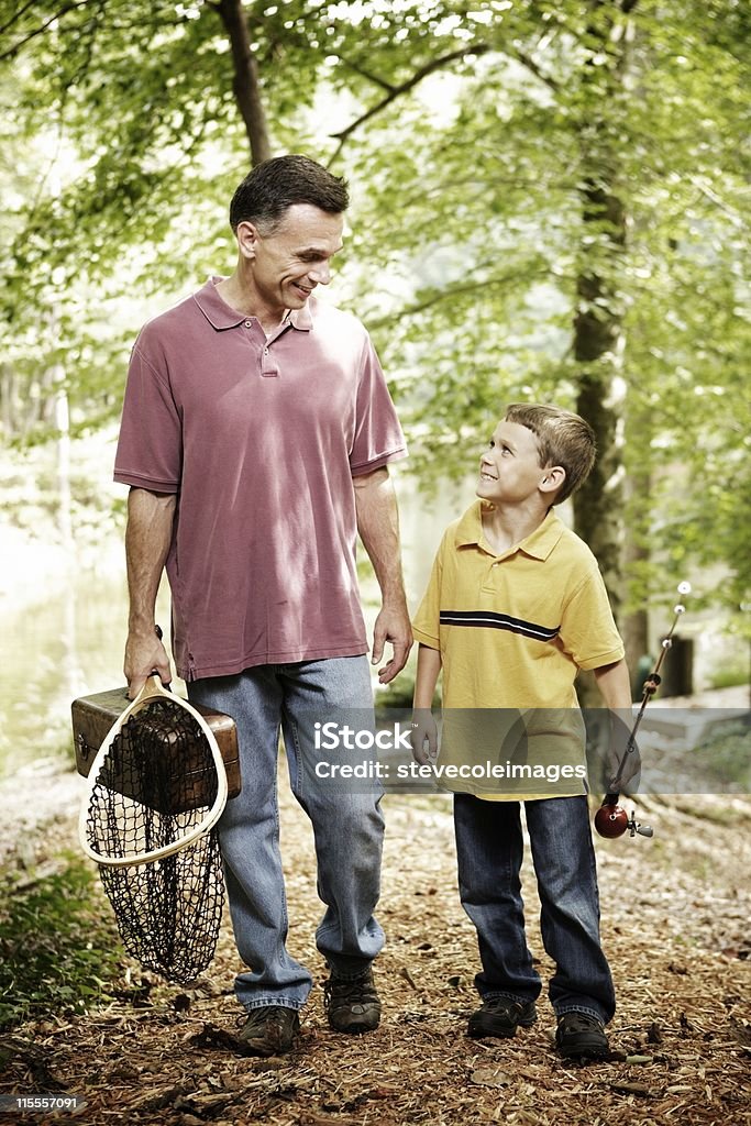 Father and Son Father and son walking through the woods carrying fishing gear. Vertical shot. Activity Stock Photo