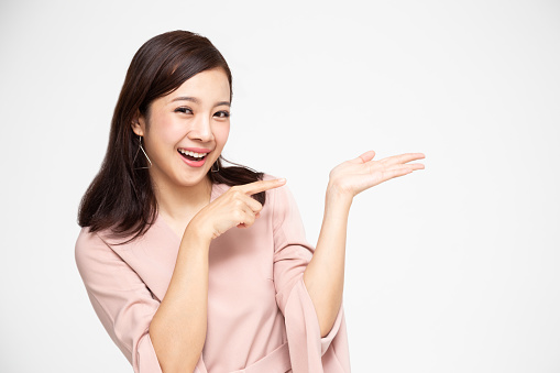 Young elegant Asian woman smiling and pointing to empty copy space isolated on white background