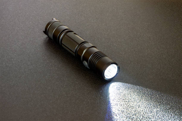 torcia a led nera metallizzata su sfondo nero. fascio di luce su sfondo materale - tactical flashlight foto e immagini stock