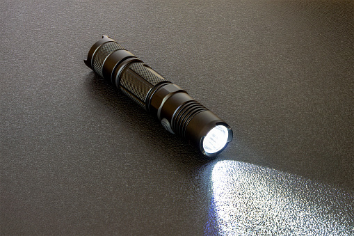 Metallic black LED flashlight on a black background. Light beam on textural background.
