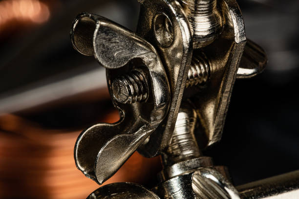 A wing nut and thumb screw securing a steel ball joint on a piece of shop equipment.  Helping hands tools are often used in soldering, macro photography and other crafts requiring the ability to hold small items steady. A wing nut and thumb screw securing a steel ball joint on a piece of shop equipment.  Helping hands tools are often used in soldering, macro photography and other crafts requiring the ability to hold small items steady. work tool nail wood construction stock pictures, royalty-free photos & images