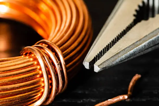 Photo of Macro Image of a coil of copper wire and a pair of needle-nose pliers.  electrician's Work tools and materials for the job featured together