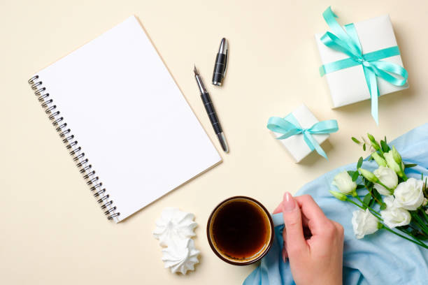 istock Flat lay feminine accessories, gift box, paper notepad, coffee cup, marshmallow, white roses flowers on pastel colors beige background. Top view beauty fashion blogger desk with diary and female stuff 1155580066