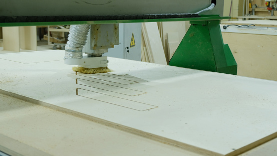 Modern woodworking machine in action. Cuts curly pieces from plywood sheet. Production of wooden furniture.