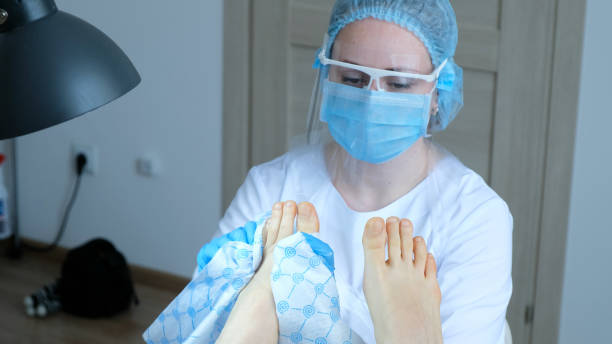 Pedicure master in a protective mask wipes a moisturizing cream from a client's foot with a paper towel A pedicure master in a protective mask wipes a moisturizing cream from a client's foot with a paper towel. welding mask stock pictures, royalty-free photos & images