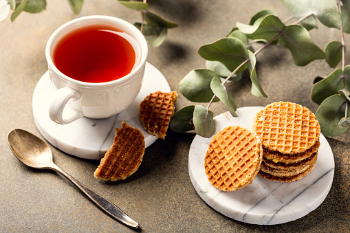 Cup of tea with mini stroopwafel, syrupwaffles cookies and eucalyptus twigs on light background.