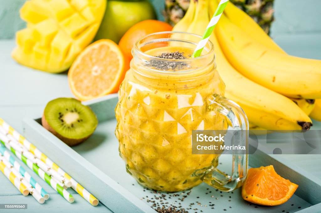 smoothie juice with chia seeds Exotic summer food concept with tropical fruits banana, orange, mango, pineapple, kiwi and yellow smoothie juice with chia seeds in glass. Antioxidant Stock Photo