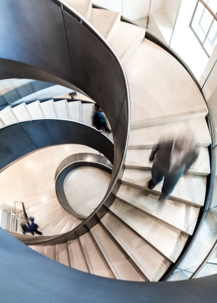istock Blurred Motion of People on Abstract Spiral Staircase 1155600170