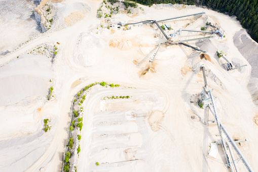 Aerial of stone crushers and sorters in a quarry landscape. Heaps of gravel and stones in the pit and many conveyor belts radiating out from the crushers.