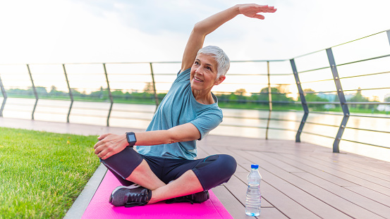 Mature woman doing yoga at park and looking away. Senior woman enjoying nature during a breathing exercise. Portrait of a fitness woman stretching arms and looking away outdoor