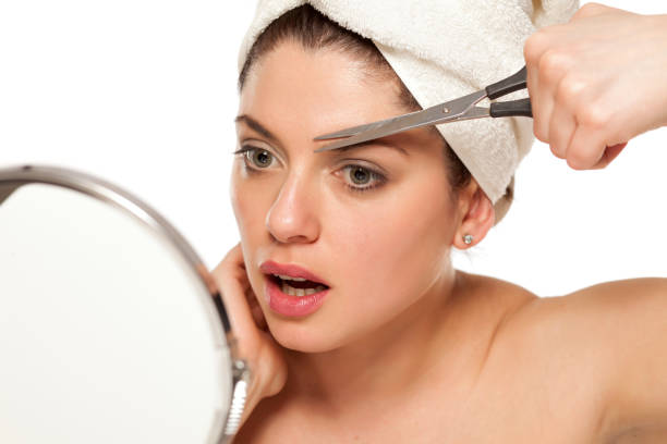 Young beautiful woman with towel on her head shape her eyebrows with scissors