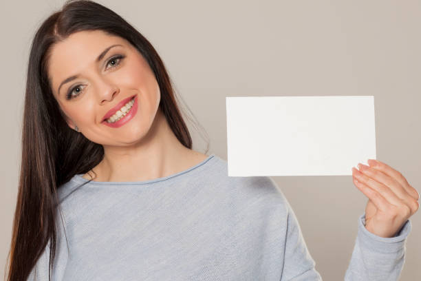 istock Smiling woman showing empty blank paper card sign with copy space for text 1155602764
