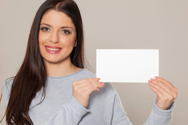 istock Smiling woman showing empty blank paper card sign with copy space for text 1155602766
