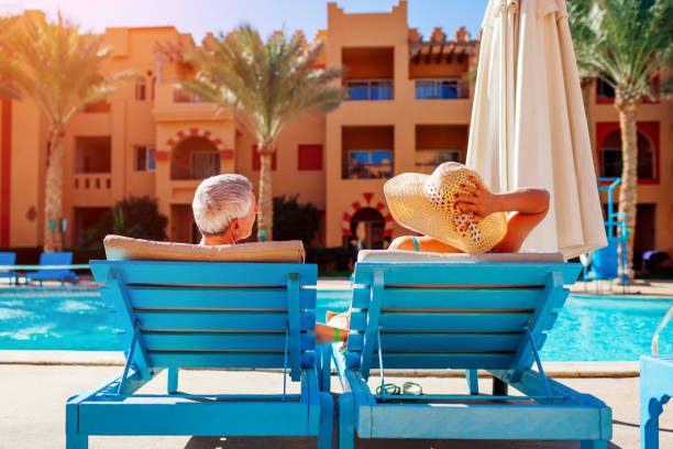pareja de la tercera edad relajándose en la piscina tumbado en chaise-longues. gente disfrutando de las vacaciones de verano. - lugar turístico fotografías e imágenes de stock