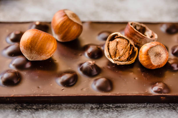 Dark chocolate with hazelnuts in the shell on gray background, closeup. stock photo