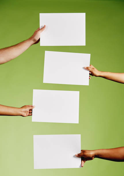 istock Four mixed hands hold blank pieces of paper against green 1155607116