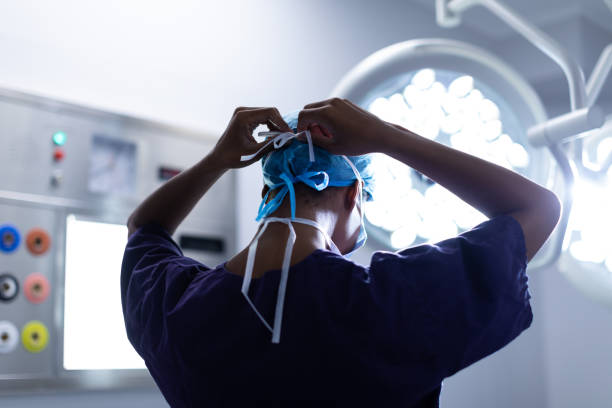 Female surgeon wearing surgical mask in operation theater at hospital Rear view of Mixed-race female surgeon wearing surgical mask in operation theater at hospital doctors surgery stock pictures, royalty-free photos & images