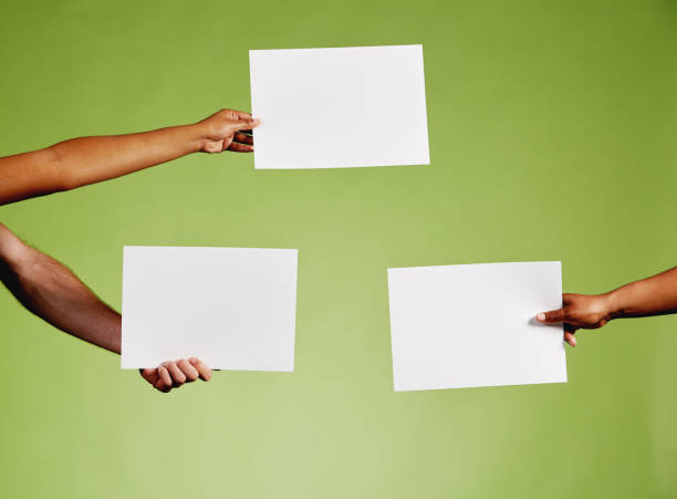 istock Three hands hold out blank sheets of paper against green 1155608336