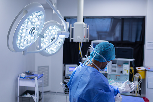 Rear view of Caucasian male surgeon wearing medical gloves in operation theater at hospital