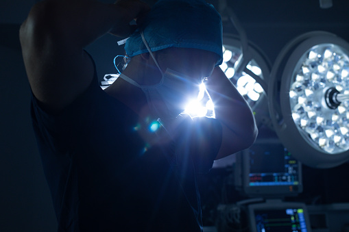 Low angle view of Caucasian male surgeon wearing surgical mask in operation theater with surgical equipment on the background at hospital.