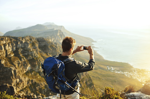 Shot of a young man taking photographs of the view while hiking up a mountain