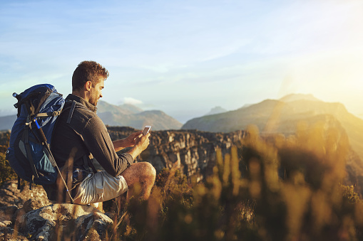 Shot of a young man using a smartphone while hiking up a mountain