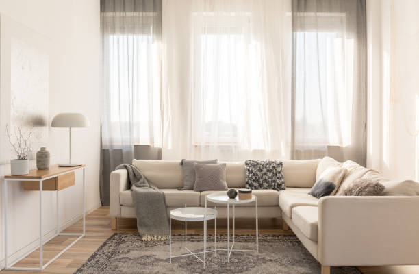 istock Beige comfortable corner sofa with grey pillows in elegant living room interior with white wall 1155613496
