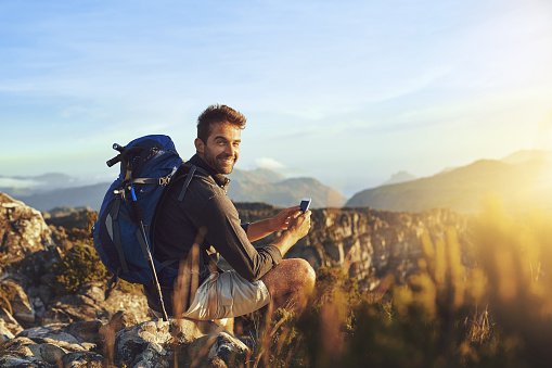 Shot of a young man using a smartphone while hiking up a mountain