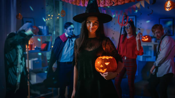 Halloween Costume Party: Gorgeous Seductive Witch Wearing Dress Holds Burning Pumpkin. Background: Beautiful Devil, Scary Death, Count Dracula, Zombie Dancing in the Decorated Room Halloween Costume Party: Gorgeous Seductive Witch Wearing Dress Holds Burning Pumpkin. Background: Beautiful Devil, Scary Death, Count Dracula, Zombie Dancing in the Decorated Room costume stock pictures, royalty-free photos & images